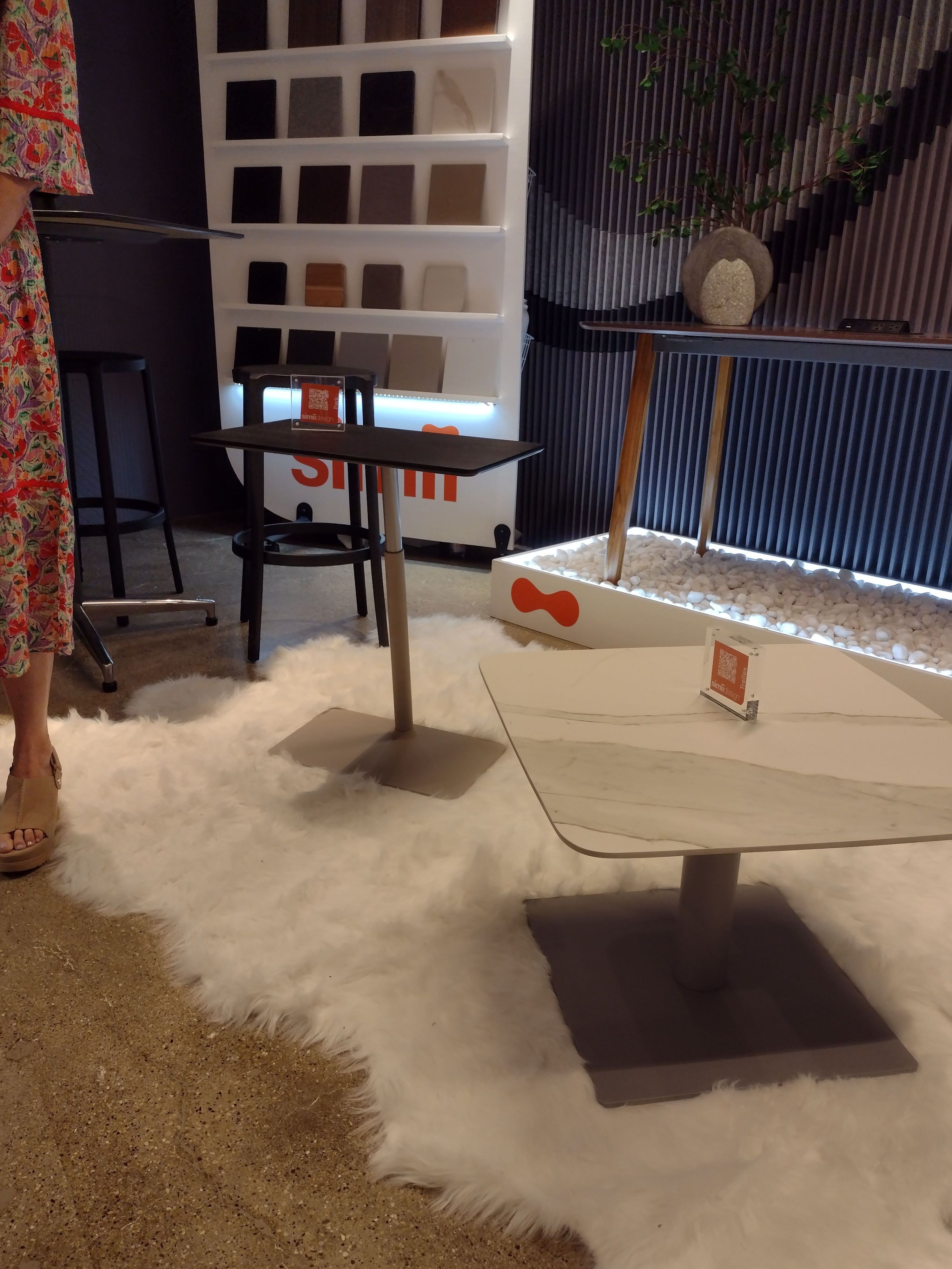 An image of some side tables on display at NeoCon 2024. These tables are adjustable in height and have natural finishes. They are placed on a white rug that is very fuzzy.
